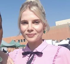 two people standing next to each other in front of a building and one is wearing a pink shirt