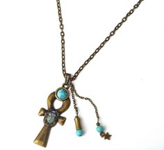 "A mystical necklace featuring a large Egyptian ankh pendant with a scarab beetle decoration, an ancient symbol of the resurrection of life, accented with painted touches of lustrous violet and turquoise! A little violet Swarovski crystal rhinestone sparkles from its back and turquoise blue magnesite beads dangle alongside the unique pendant! A faux turquoise stone sits at the top of the ankh pendant as yet another design element. The luck-bringing pendant dangles from a sturdy antiqued gold cha Symbolic Ankh Necklace Adjustable, Symbolic Ankh Necklace, Spiritual Ankh Jewelry With Large Pendant, Amulet Style Ankh Necklace In Brass, Bronze Ankh Bohemian Jewelry, Bohemian Ankh Bronze Jewelry, Bronze Bohemian Cross Necklace, Bohemian Bronze Cross Necklace, Bronze Cross Bohemian Necklace