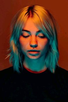 a woman with blonde hair and blue eyes looks down at her cell phone while wearing a black t - shirt