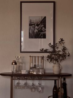 a shelf with wine glasses and bottles on it in front of a framed black and white photograph