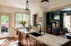 a kitchen with marble counter tops and an island in front of two windows that look out onto the backyard