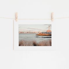 a photo hanging on a clothes line next to a body of water with buildings in the background