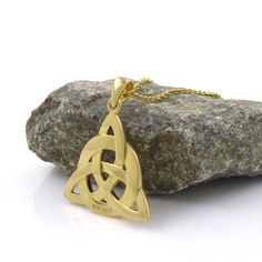 a gold necklace with an intertwined knot on it, sitting next to a rock