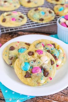 chocolate chip cookies with m & m candy in the middle on a white plate next to a cooling rack