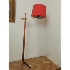 a lamp that is on top of a wooden floor next to a wall with a red shade