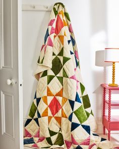 a quilted blanket sitting on top of a floor next to a pink table lamp