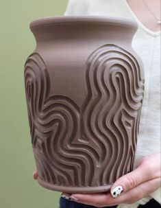 a woman holding a large vase with wavy designs on it's face and hands