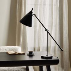 a desk lamp sitting on top of a wooden table next to a book and cup