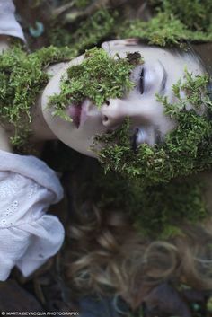 a woman is covered in green moss and has her eyes closed while laying down on the ground