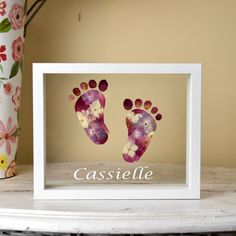 a baby's hand and foot prints are displayed in a white frame on a table