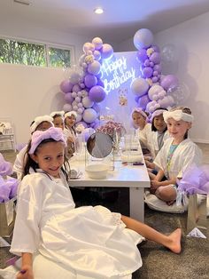 a group of children sitting on the floor in front of a table with purple balloons