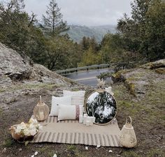 an outdoor seating area with pillows and other items on the ground in front of a lake