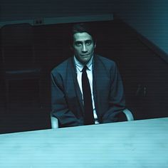 a man in a suit and tie sitting at a table with his hands on his hips