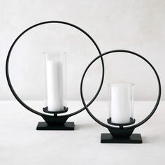 two white candles sitting on top of black metal stands next to each other with one candle in the middle