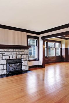 an empty living room with hard wood flooring and stone fireplace in the center area