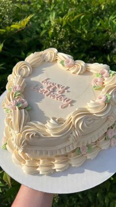 a white cake with pink flowers and the words happy birthday on it is being held by someone's hand