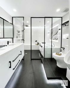 a modern bathroom with black and white flooring, glass partitions, double sinks, and two toilets