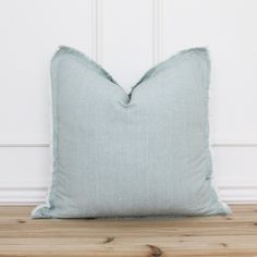 a light blue pillow sitting on top of a wooden floor next to a white wall