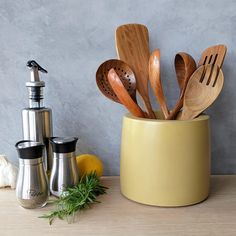 wooden utensils and spoons in a yellow container on a table next to salt and pepper shakers