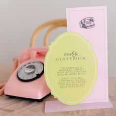 a pink phone sitting on top of a wooden table next to a card with an old fashioned telephone