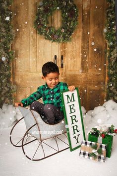 a young boy sitting in a sleigh with a merry sign next to him