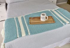 a coffee cup is sitting on the edge of a bed with a blue and white blanket