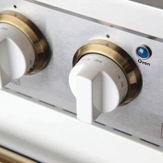 two knobs on the front of a stove top oven with brass trim and white handles