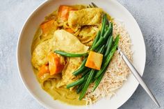 a white bowl filled with green beans, rice and chicken curry next to a fork