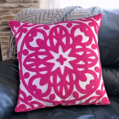 a pink and white pillow sitting on top of a black leather couch next to a brick wall