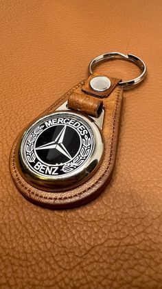 a keychain with a mercedes emblem on it sitting on a leather surface,