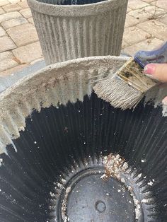 a person holding a paintbrush over a black pot with dirt on the bottom and side