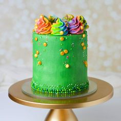 a green cake with rainbow frosting and sprinkles sits on a gold plate