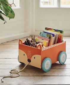 a wooden toy cart filled with books on top of a hard wood floor next to a potted plant