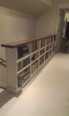 a bookshelf filled with lots of books on top of a white floor next to a stair case