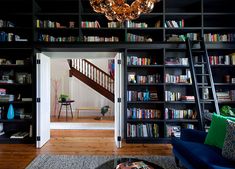 a living room filled with lots of furniture and bookshelves next to a stair case