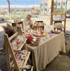 a woman sitting at a table covered in lots of cupcakes and pastries