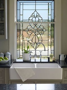 a white sink sitting under a window next to a bowl of fruit on top of a counter