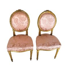 two pink chairs sitting next to each other on top of a white surface with gold trimming