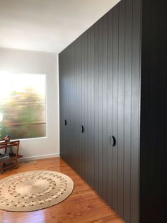 an empty room with wooden floors and black cupboards on the wall next to a rug