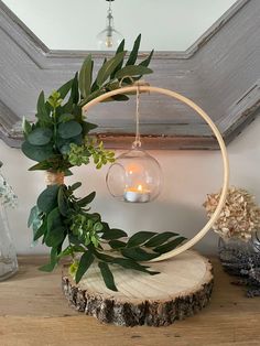 a wooden table topped with a glass ball filled with greenery next to a candle