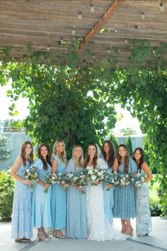 a group of women standing next to each other under a pergolated roof holding bouquets