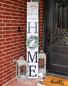 a welcome to our home sign next to two lanterns on the front porch with greenery