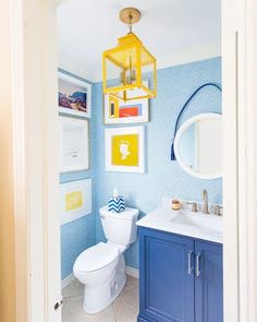 a bathroom with blue and yellow decor on the walls, white tile flooring and a hanging light fixture