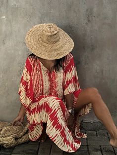 a woman in a red and white dress sitting on the ground wearing a straw hat