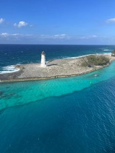 an island with a light house on it in the middle of the ocean, surrounded by blue water