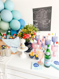 a table topped with lots of bottles and glasses filled with drinks next to balloons in the background