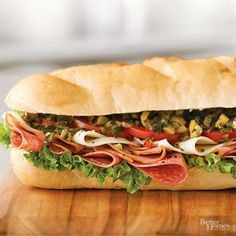 a sub sandwich with meat, lettuce and tomatos on a wooden cutting board