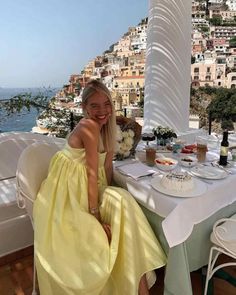 a woman in a yellow dress sitting at a table with food and drinks on it