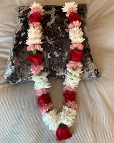 a decorative letter made out of flowers on top of a bed with a pillow behind it