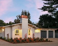 a small white house with two garages and trees in the background at night time